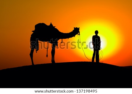 Rajasthan village. Silhouette of a man and camel at sunset in the desert, Jaisalmer - India