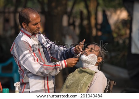 HARIDWAR, INDIA - NOVEMBER 8, 2012: An unidentified street barber shaving a man using an open razor blade on a bank of sacred river Ganges in Haridwar. Poor Indians flock to Haridwar for charity.