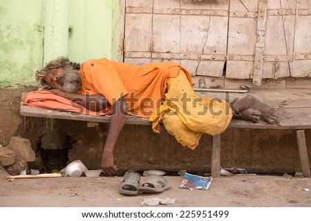 PUSHKAR, INDIA - OCTOBER 24, 2014: Unidentified Indian homeless man sleeps  near the ghat along the sacred Sarovar lake. Poor Indians flock to Pushkar for charity.