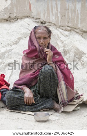 LEH, INDIA - JUNE 24, 2015: Unknown poor woman begs for money from a passerby on the street in Leh, Ladakh. Poverty is a major issue in India