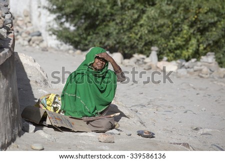 LEH, INDIA - SEPTEMBER 08, 2014: Unknown poor woman begs for money from a passerby on the street in Leh, Ladakh. Poverty is a major issue in India