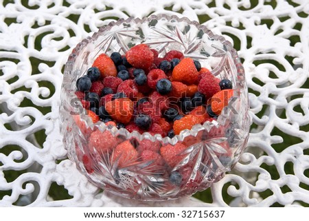 A bowl of mixed summer fruits sitting on a white outdoor table