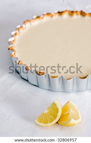 A baked lemon tart on a white tablecloth with lemons