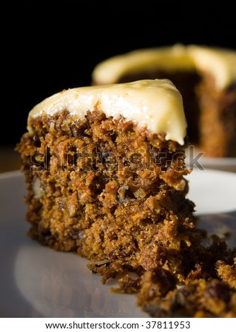 Closeup of a piece of carrot cake on a plate with short depth of field. Cake slice on a plate, with whole cake in the background.