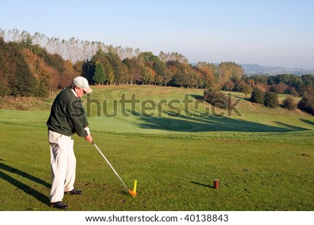 A senior golfer teeing off with a driver on a golf course in England in early autumn. Photo taken at point of contact, with motion blur on the golf ball.