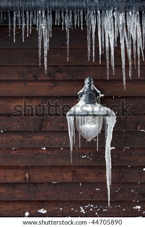 Long icicles hanging from an outdoor lamp and drainpipe in winter.