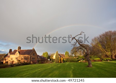 A rainbow over a traditional manor house and garden in England in winter. Cloudy sky overhead with copyspace for your text/design.