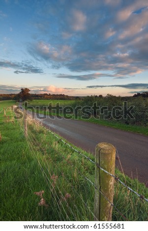 A barbed-wire fence running alongside a typical country road in rural Warwickshire, England, with sunset sky in the background.