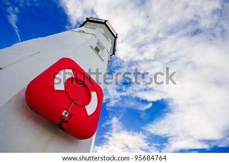 White lighthouse with a red life preserver against a cloudy blue sky on a bright winter morning. Photo taken in Anstruther, Scotland.