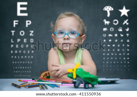 Smart kid sitting at a table with glasses on the background of the table for an eye examination