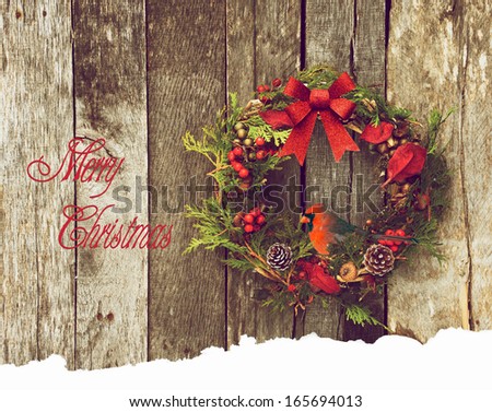 Christmas card design with a Christmas wreath with a beautiful Northern cardinal perched, hanging on a rustic wooden wall with text-Merry Christmas.