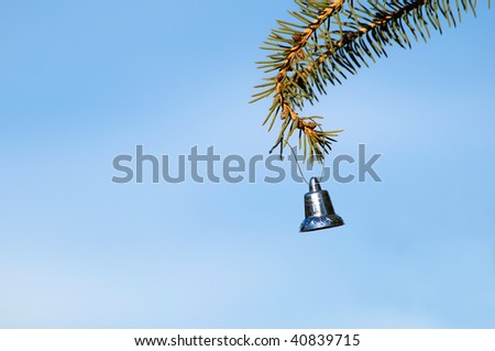 Christmas.  Silver bell hangs on a pine branch against a brilliant November sky.