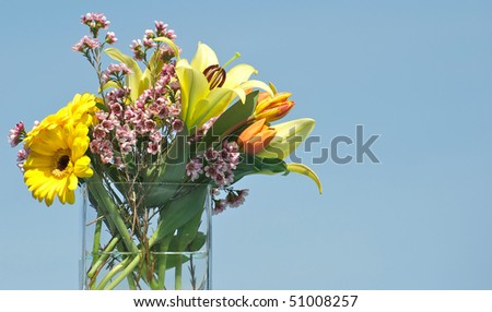 Spring flowers in a glass vase against a brilliant blue sky with room for text.