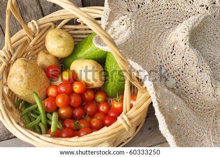 Close up image of a basket of freshly picked vegetables and a gardener\'s straw hat.