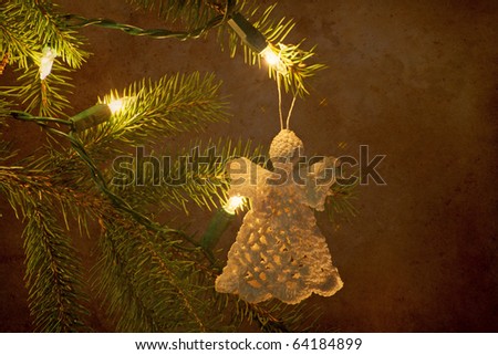 Lace angel Christmas decoration hanging from a pine branch with lights and copy space.
Grunge textured.