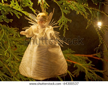 Christmas angel decoration hangs from a  branch illuminated  by the twinkling lights of the Christmas tree on a dark winter night with copy space.