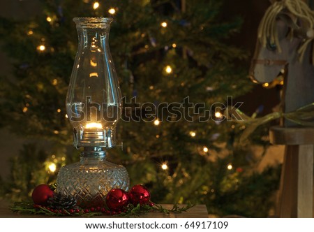 Christmas scene featuring a lit oil lamp on a table in front of a Christmas tree with sparkling lights and a toy wooden pony.