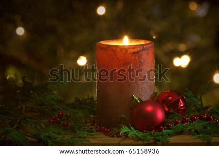 Christmas candle with a light textured background with beads, Christmas balls and cedar sprigs with sparkling lights on the Christmas tree in the background.