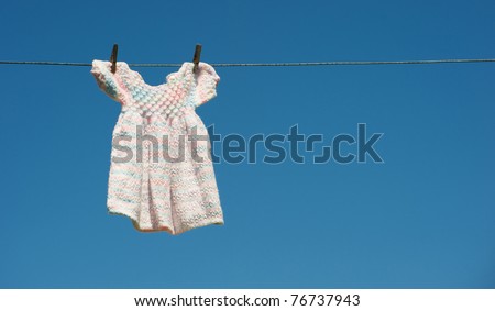 A hand knitted baby dress hangs drying on a clothesline against a brilliant blue sky with copy space.