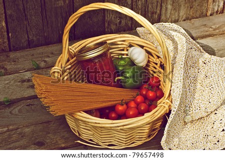 A basket of freshly picked organic vegetables, homemade pasta sauce and raw whole wheat pasta on a wooden backdrop.