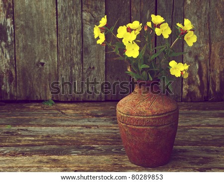 Richly colored moody vintage style image of beautiful evening primrose flowers in a rustic vase on a grunge wood backdrop with copy space.