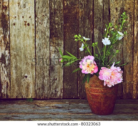 Pink and white flowers in a rustic vase on a grunge wood backdrop with copy space.