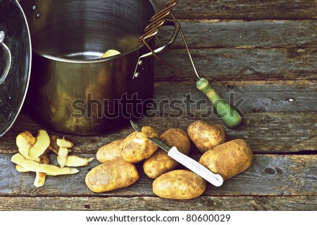 Richly colored moody vintage style close up image of potatoes, a knife, old fashioned potato masher and pot on grunge wooden backdrop with copy space.