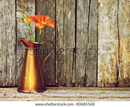 A day lily in an antique copper vase on a rustic wood backdrop with copy space.