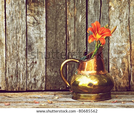 A single lily in an antique copper vase on a rustic wood backdrop with copy space.