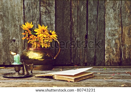 Brown eyed Susan flowers in an antique copper vase and an old book,  and antique candle holder on a rustic wood backdrop with copy space.
