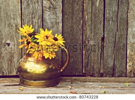 Brown eyed Susan flowers in an antique copper vase on a rustic wood backdrop with copy space.