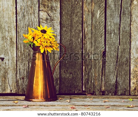 Brown eyed Susan flowers in an antique copper vase on a rustic wood backdrop with copy space.