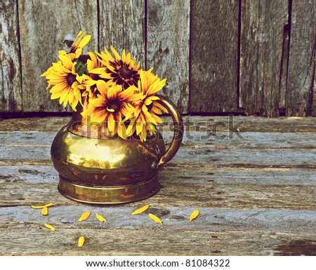 Brown eyed Susan flowers in an antique copper vase on a grunge wood backdrop with copy space.