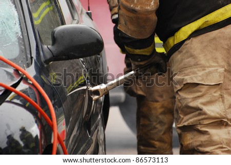 Fireman in motion prying open the door of a car which has been involved in a serious accident.  Selective focus on the fireman\'s arm and hand.  Part of a series.