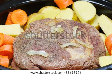 Crock pot with fresh free range organic and locally purchased beef blade roast lightly browned with onions, seasonings, golden potatoes and carrots  ready for slow cooking.