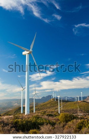 Wind Turbines generating electricity on a remote hillside in Southern Europe. Bright blue sky background with few white clouds. Portrait Format
