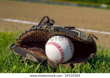 A youth baseball glove and ball laying on the grass next to the infield.