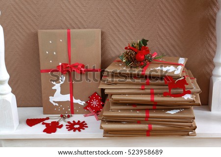 Many books as Christmas gifts, wrapped and homemade decorated, piled on white wooden console table. Handmade painting of deer on a parcel. Side view.