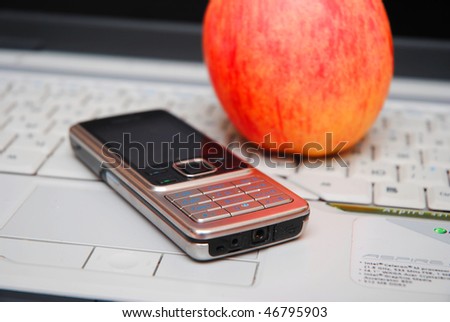 silver mobile phone and red apple over grey laptop