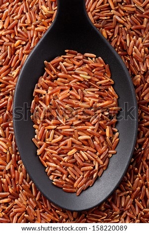 Top view of black spoon full of long grain red rice