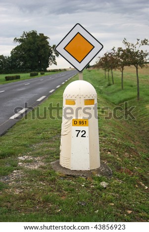 French road sign and bollard with road and trees in background