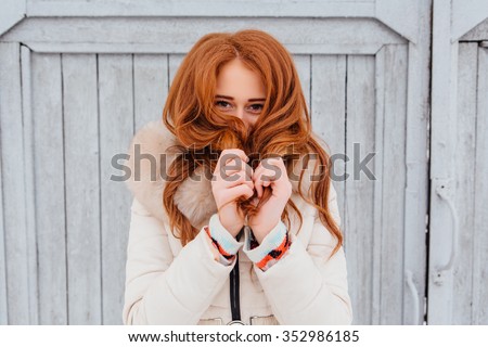 Portrait of a beautiful red hair young woman in warm clothes outdoor on the grey wooden background. Girl shows different emotions.