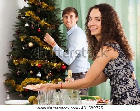 Young happy family couple decorating Christmas tree and serving  festive table