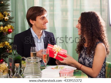 Woman presenting gift to man at table during  dinner at home