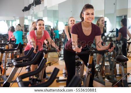vigorous females riding stationary bicycles in modern gym for women