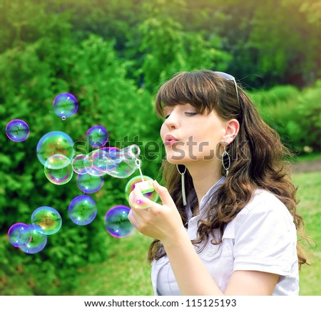 romantic young girl inflating colorful soap bubbles in spring park