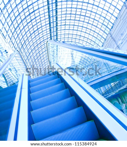 Wide angled view to perspective escalators stairway inside contemporary blue glass business centre, concept of successful career elevation