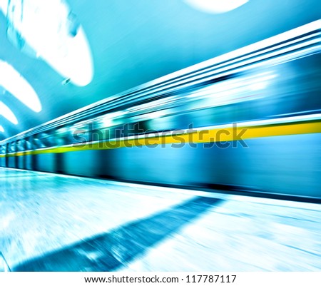 Perspective wide angle view of modern light blue illuminated and spacious public metro marble station with fast blurred trail of train in vanishing traffic motion