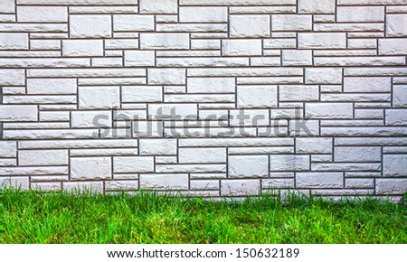 Weathered texture of stained old dark brick wall background, grungy rusty blocks of stone-work technology, white horizontal architecture with bright green grass outdoor in the park