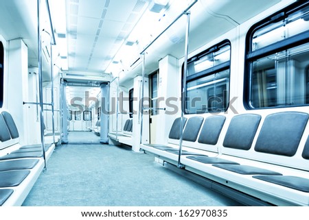 Perspective and diminishing wide angle view to Contemporary blue spacious interior and comfortable seats of modern train empty light illuminated wagon moving fast inside urban vanishing metro tunnel